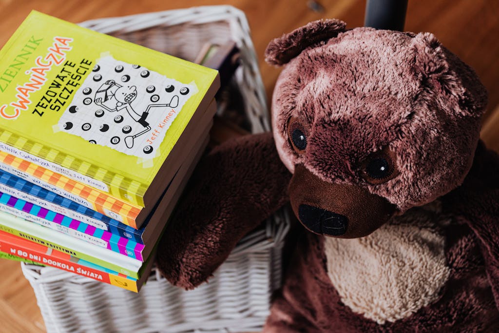 A stack of colorful children's books next to a plush teddy bear in a cozy kids' room.